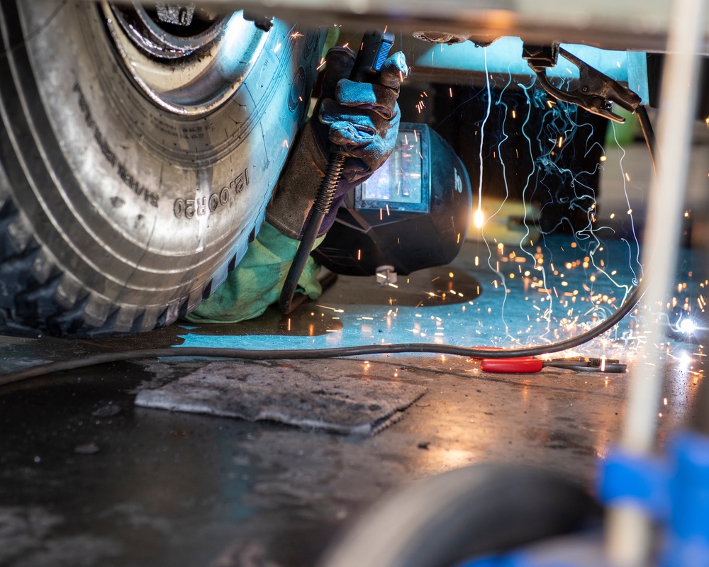 A realistic vehicle maintenance worker performing undercarriage maintenance.